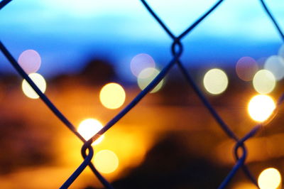Defocused image of illuminated chainlink fence against sky at night