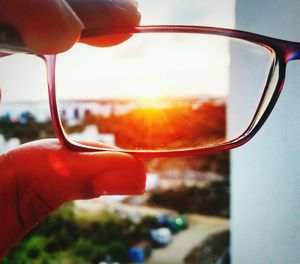 Close-up of person holding sunglasses against sky during sunset