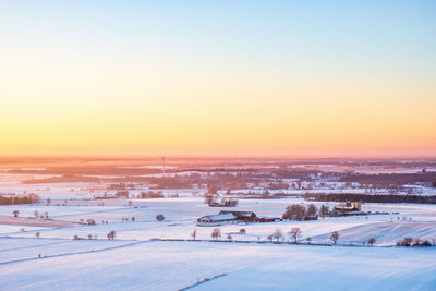 Snow covered field against sky during sunset