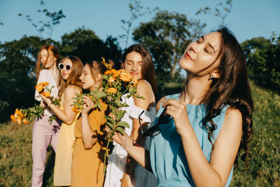 Smiling beautiful women holding flowers standing at park
