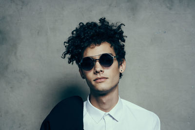 Portrait of young man wearing sunglasses standing against wall