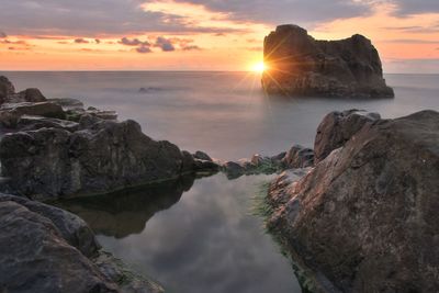 Rocks on sea shore against sky during sunset