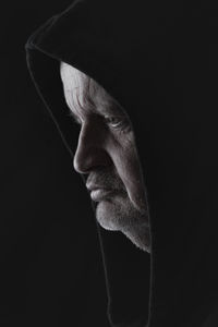 Close-up of man wearing hood against black background