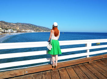 Full length rear view of woman on pier by sea against clear blue sky