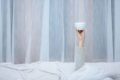 Midsection of woman with arms crossed on bed at home