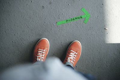 Low section of person standing by arrow sign with text on footpath