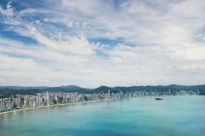 View of city at waterfront against cloudy sky