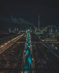 High angle view of illuminated railroad tracks amidst buildings in city at night