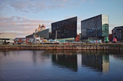 Buildings by river against sky in city