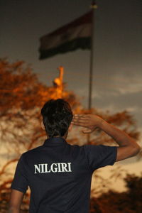 Rear view of man saluting flag during sunset