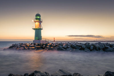 Lighthouse by sea against sky during sunset