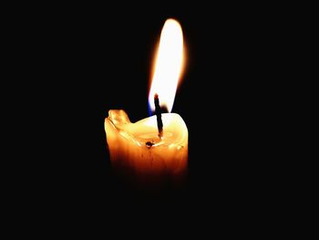 Close-up of burning candle against black background