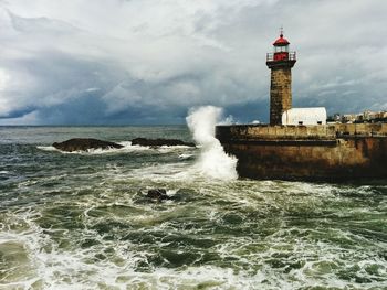 Lighthouse on beach against cloudy sky