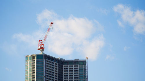 Low angle view of crane by building against sky