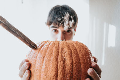 Portrait of man holding pumpkin against wall