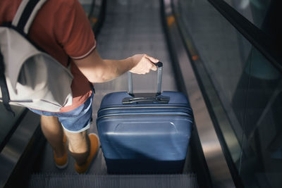 Traveler at airport terminal. rear view of man with suitcase and backpack standing on ecalator. 