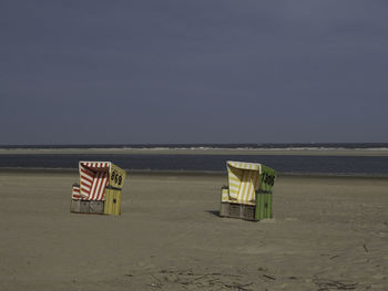 Hooded chairs on beach against sky