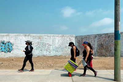 Rear view of people walking against wall in city