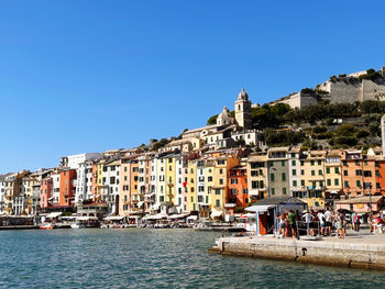 Buildings by river against clear blue sky
