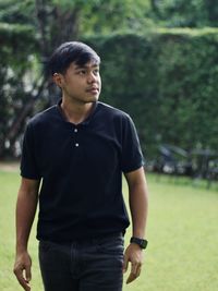 Young man looking away while standing against trees