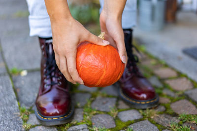 Close up of hands and boots of a young woman, who lifts up an orange pumpkin.