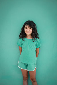 Portrait of smiling girl in green t-shirt and shorts against green wall