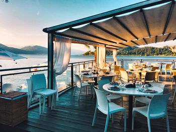 Chairs and tables in restaurant by sea against sky