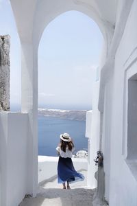 Rear view of woman standing by sea against building