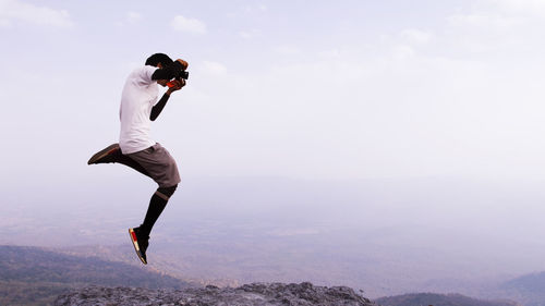 Man jumping on mountain against sky