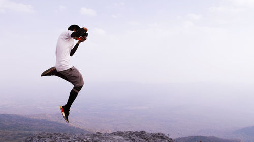 Man photographing while jumping against sky