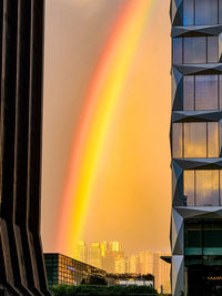 Low angle view of rainbow over buildings against sky during sunset