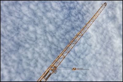 Low angle view of crane against cloudy sky