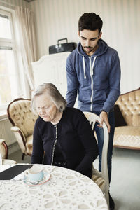 Young caretaker adjusting chair for senior woman in living room at nursing home