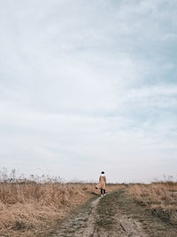 Rear view of woman walking on field against sky