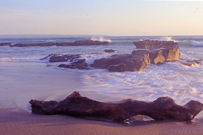 Rocks on shore against sky during sunset