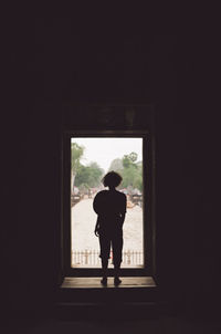 Rear view of silhouette of woman standing at doorway in darkroom