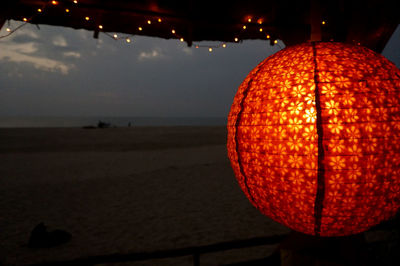 Close-up of illuminated lantern hanging by sea against sky at night