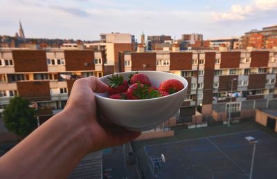 Close-up of hand holding bowl against buildings in city