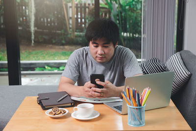 Young woman using mobile phone while sitting on table