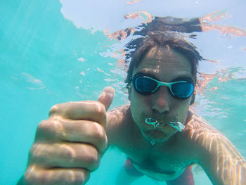 Portrait of shirtless man gesturing thumbs up in turquoise sea