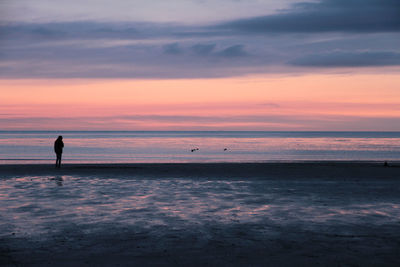 Silhouette man standing on beach against sky during sunset