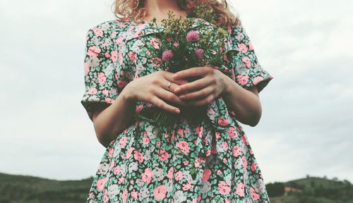 Midsection of woman holding bouquet while standing against sky