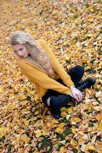 High angle view of young woman sitting on yellow leaves during autumn