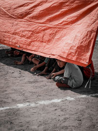 Low section of little boy hiding behind a red tarp