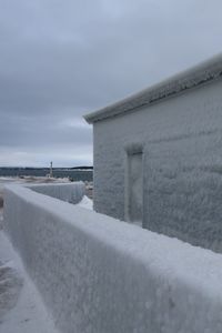Snow covered land by sea against sky