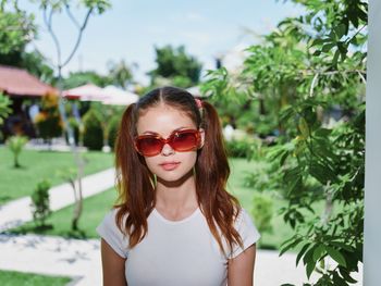 Portrait of young woman wearing sunglasses standing against trees