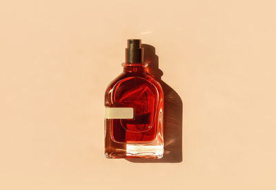 Transparent perfume bottle with red filling on a pastel beige background in the sunlight. flat lay