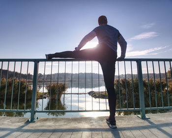 Rear view of man standing by railing against sky