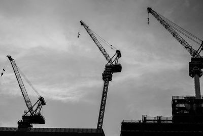 Low angle view of cranes at construction site against sky