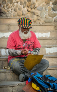 Senior man tying clipboard while sitting on steps